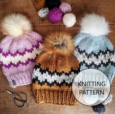 three knitted hats with pom - poms and scissors on a wooden surface