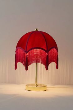 a red table lamp with tassels on the base and a white wall behind it