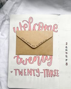 an open notebook with a brown envelope and pink lettering on the cover that says welcome twenty - three