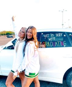 two girls standing in front of a white car with the words get in user were graduating written on it