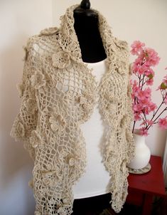 a crocheted shawl on a mannequin next to a vase with pink flowers