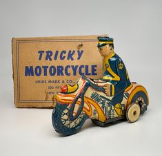 a toy motorcycle with a man on it next to a cardboard box that says tricky motorcycle