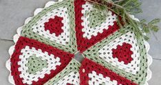 a crocheted doily with red, green and white designs on it sitting on the ground