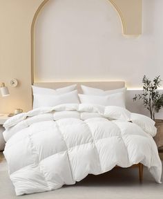 a bed with white comforter and pillows in a room next to a potted plant