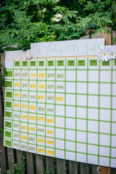 a green and white checkered calendar on a wooden fence with daisies in the foreground