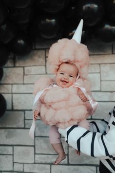 a woman holding a baby wearing a pink unicorn costume