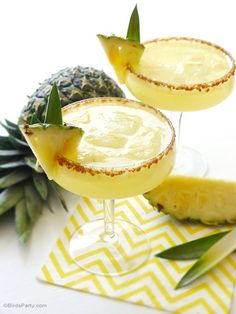 two margaritas with pineapple garnish sit on a yellow and white napkin