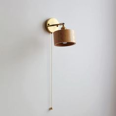 a wall lamp with a wooden shade hanging from it's side on a white wall