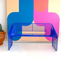 a blue bench sitting next to a potted plant in front of a colorful wall