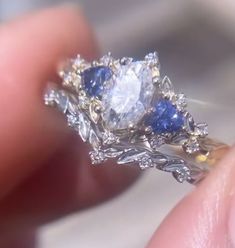 a close up of a person's hand holding a diamond and sapphire ring