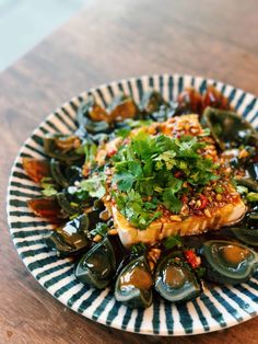 a white and blue plate topped with fish covered in green vegetables on top of a wooden table