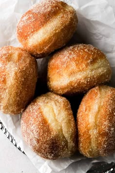 several sugared donuts sitting in a basket on top of white paper with a spoon next to it