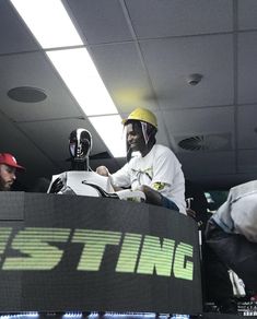 two men sitting in the back of a truck with helmets on and one man wearing a yellow helmet