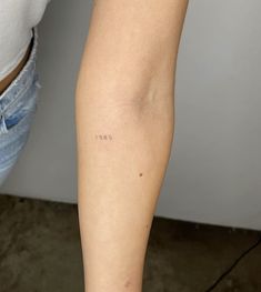 a person with a small tattoo on their arm and leg, standing next to a wall