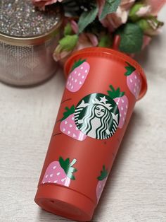 a red starbucks cup sitting on top of a table next to a vase filled with flowers