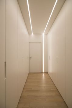 an empty hallway with white walls and wooden floors is lit by recessed lighting on the ceiling