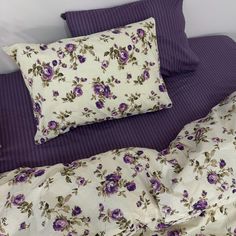 a bed with purple and white flowers on the comforter, pillows and pillow cases