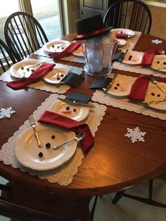 a wooden table topped with white plates covered in snowman napkins and place mats