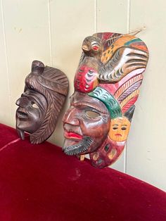 two african masks sitting on top of a red velvet bench next to a white wall