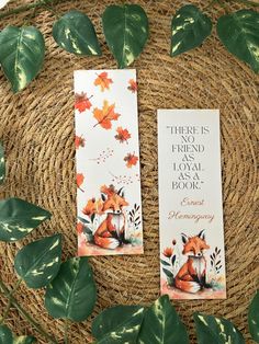 two bookmarks sitting on top of a wicker basket next to some green leaves