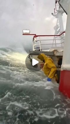 a man in yellow jacket standing on top of a boat next to the ocean with large waves