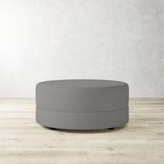 a round ottoman sitting on top of a hard wood floor next to a white wall