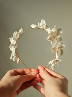 two hands are holding a white flower headpiece in the shape of a circle with flowers on it