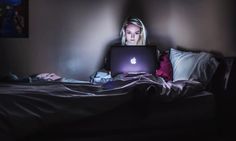 a woman sitting on her bed with an apple laptop computer in front of her face