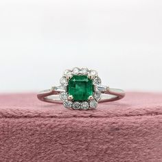 an emerald and diamond ring sitting on top of a pink velvet box with white background