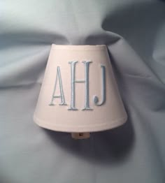 a lamp shade with the letters ahj on it sitting on a blue sheeted bed