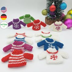 crocheted christmas sweaters are arranged in front of a small tree and ornaments