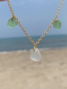 a person is holding a necklace with sea glass charms on it and the ocean in the background