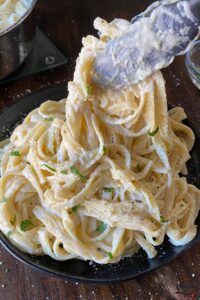 a plate full of pasta and sauce being stirred with a plastic spatula on a wooden table