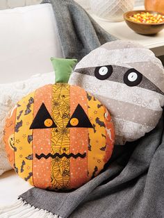 two decorative pumpkins sitting on top of a couch next to a bowl of corn