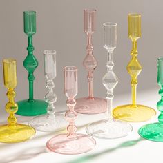 many different colored glass goblets lined up on a white surface with shadows in the background