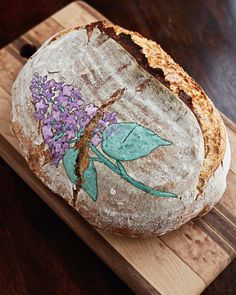 a loaf of bread sitting on top of a wooden cutting board with flowers painted on it