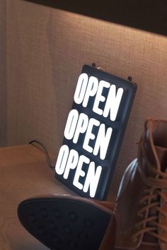 an open sign sitting on top of a wooden table next to some shoes and a lamp