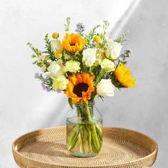 a vase filled with yellow and white flowers on top of a wicker table next to a wall