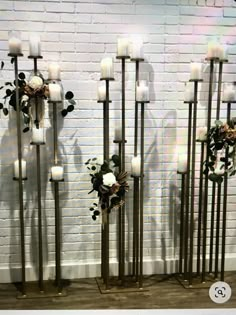 four tall metal candles with flowers and greenery on them in front of a white brick wall