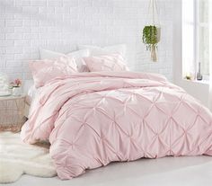 a bed with pink comforter and pillows in a room next to a white brick wall