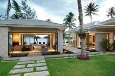 the house is surrounded by palm trees and lawns, with an ocean view in the background