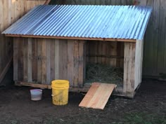 a wooden shed with a metal roof next to a yellow bucket