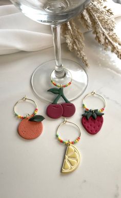 wine glass charms with fruit on them sitting next to a wine glass filled with water