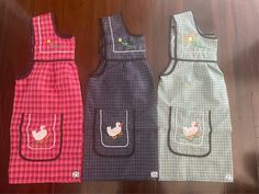 three aprons with chicken appliques on them sitting on a wooden floor next to each other