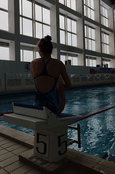 a woman sitting on the edge of a swimming pool looking out at an empty pool