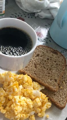 scrambled eggs and toast on a plate next to a cup of coffee