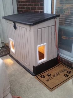 a dog house with its door open on the front porch next to an entrance mat