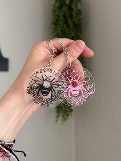 a hand holding two key chains with different designs on them, one is pink and the other is black