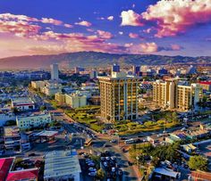 an aerial view of a city with tall buildings and mountains in the background at sunset