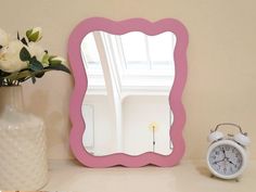 a pink mirror sitting on top of a table next to a vase with white flowers